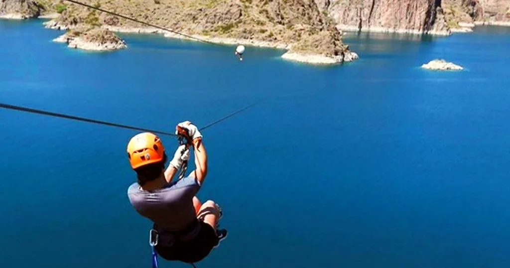 Turista disfrutando la tirolesa con vista aérea al lago Los Reyunos.